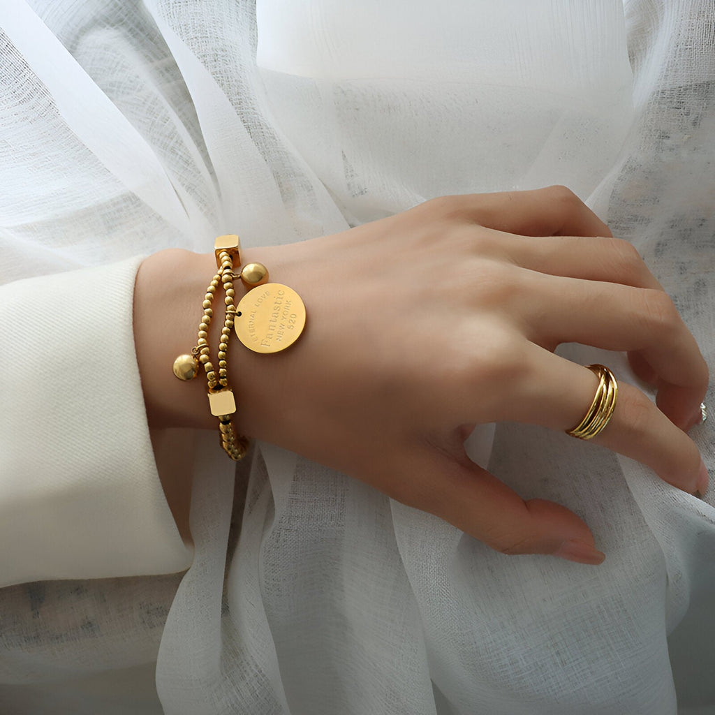 Bracelet en titane plaqué or avec perles dorées et médaillon rond porté au poignet.