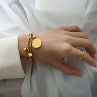 Bracelet en titane plaqué or avec perles dorées et médaillon rond porté au poignet.