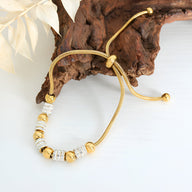 Bracelet fin en titane plaqué or avec perles dorées et cristaux scintillants, fermoir coulissant ajustable.