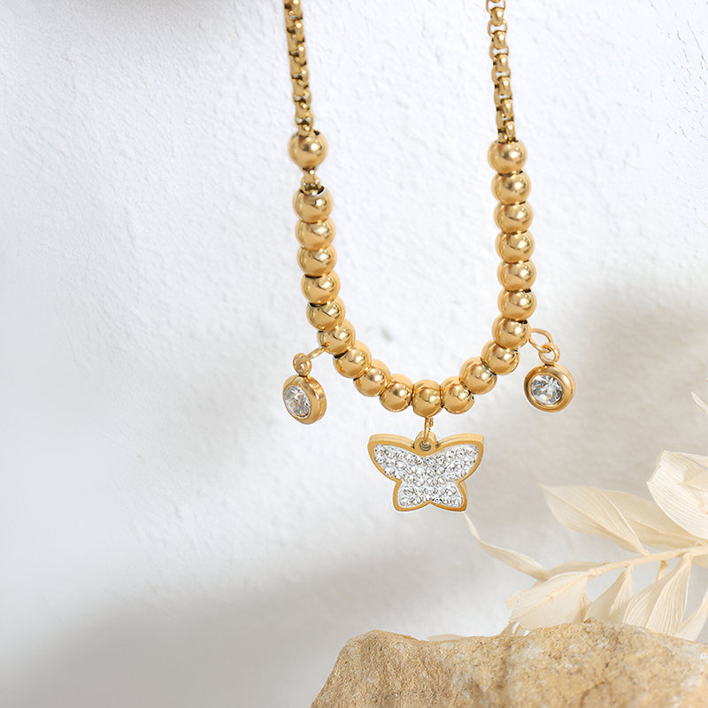 Bracelet en titane plaqué or avec perles dorées et médaillon papillon orné de pierres blanches.