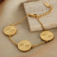 Bracelet en titane plaqué or avec trois médaillons rayonnants et chaîne délicate ajustable.