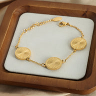 Bracelet en titane plaqué or avec trois médaillons ronds gravés motifs rayonnants sur chaîne fine.
