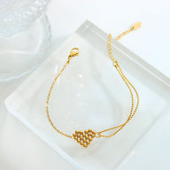 Bracelet fin en titane plaqué or avec motif cœur perlé et chaîne délicate.