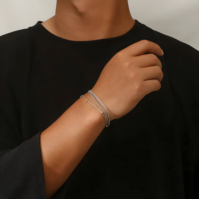 Bracelet triple en titane argenté fin et élégant porté au poignet d'un homme vêtue d'un haut noir.