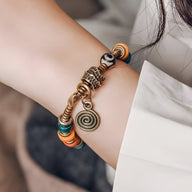 Bracelet en cuivre avec perles en verre multicolores et pendentif spirale porté au poignet féminin.