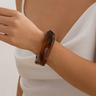 Bracelet épais en acrylique marron translucide, modelé avec des courbes lisses, porté sur poignet féminin.