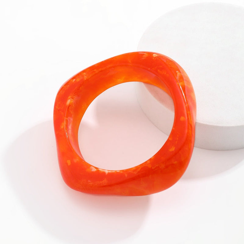 Bracelet épais en acrylique orange vif avec forme légèrement irrégulière et finition brillante.