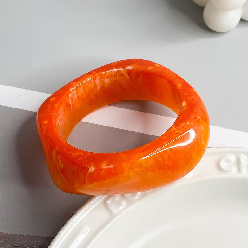 Bracelet épais en acrylique orange marbré avec forme géométrique élégante.