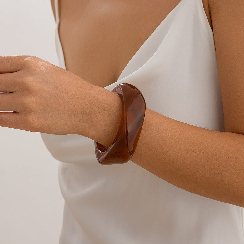 Bracelet épais en acrylique marron brillant, design torsadé, porté au poignet, style contemporain.