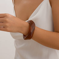 Bracelet épais en acrylique marron brillant, design torsadé, porté au poignet, style contemporain.