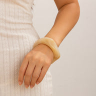 Bracelet épais beige en acrylique avec finition lisse porté au poignet féminin.