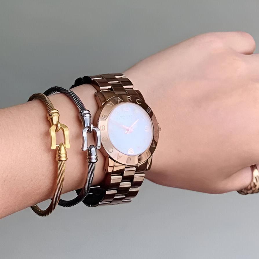 Bracelet fer à cheval en acier inoxydable noir avec petits clochettes dorées porté au poignet féminin.