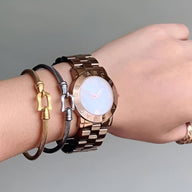 Bracelet fer à cheval en acier inoxydable noir avec petits clochettes dorées porté au poignet féminin.