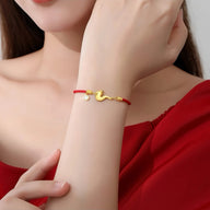 Bracelet fil rouge porte-bonheur avec motif dragon doré sur poignet féminin en robe rouge.