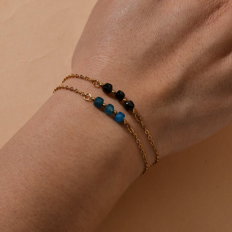 Bracelet fin en acier doré à maille forçat avec trois pierres semi-précieuses facettées, bleu et noir, élégant et lumineux.