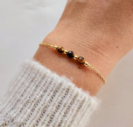 Bracelet fin en acier doré avec maille forçat et trois pierres semi-précieuses facettées noires et dorées.