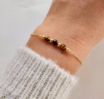 Bracelet fin en acier doré avec maille forçat et trois pierres semi-précieuses facettées noires et dorées.