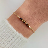 Bracelet fin en acier doré avec maille forçat et trois pierres semi-précieuses facettées noires et dorées.