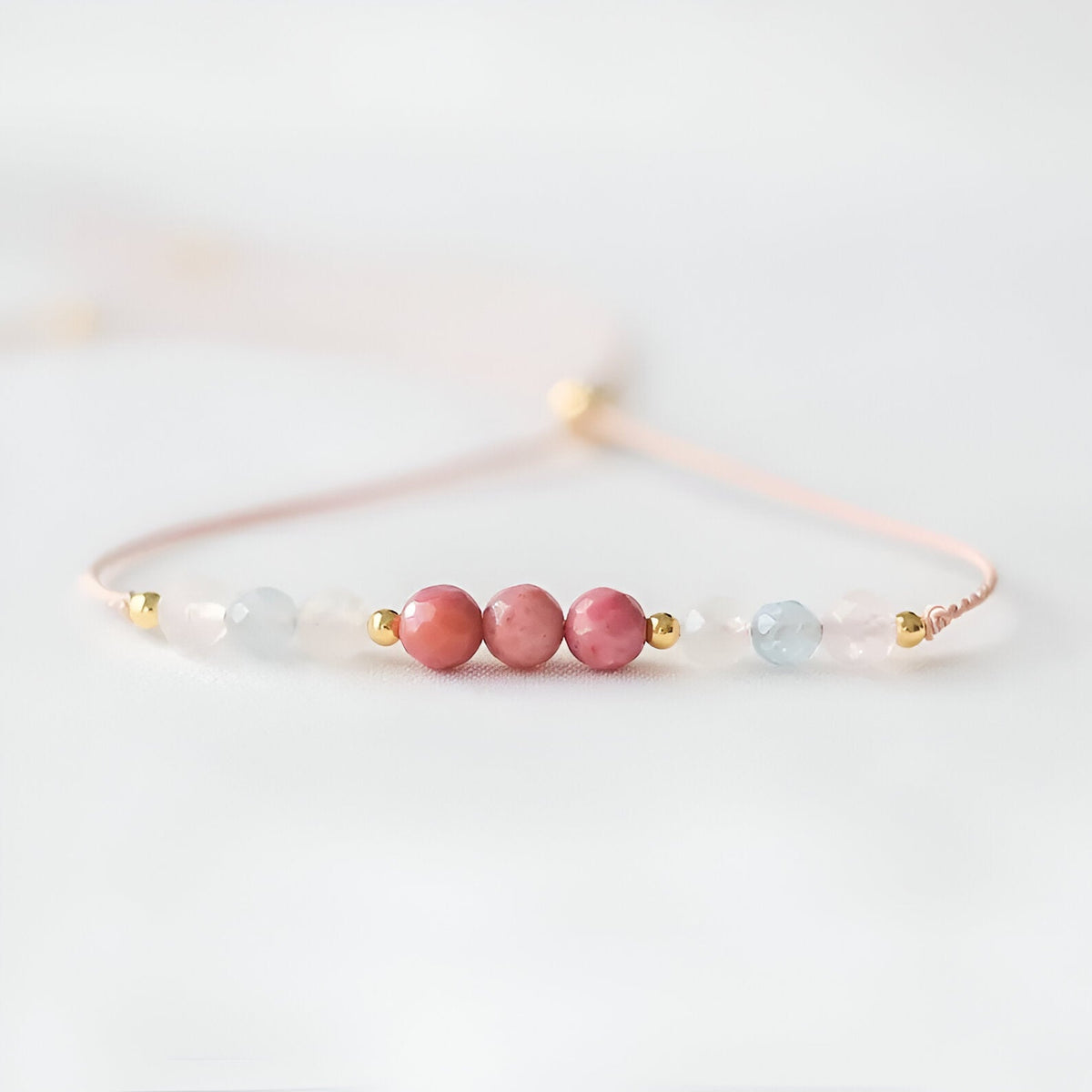 Bracelet fin en pierres naturelles rose et bleu clair avec perles dorées sur fil délicat rose pâle.