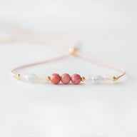 Bracelet fin en pierres naturelles rose et bleu clair avec perles dorées sur fil délicat rose pâle.