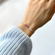 Bracelet fin rose avec petites pierres naturelles blanches et roses sur poignet féminin.