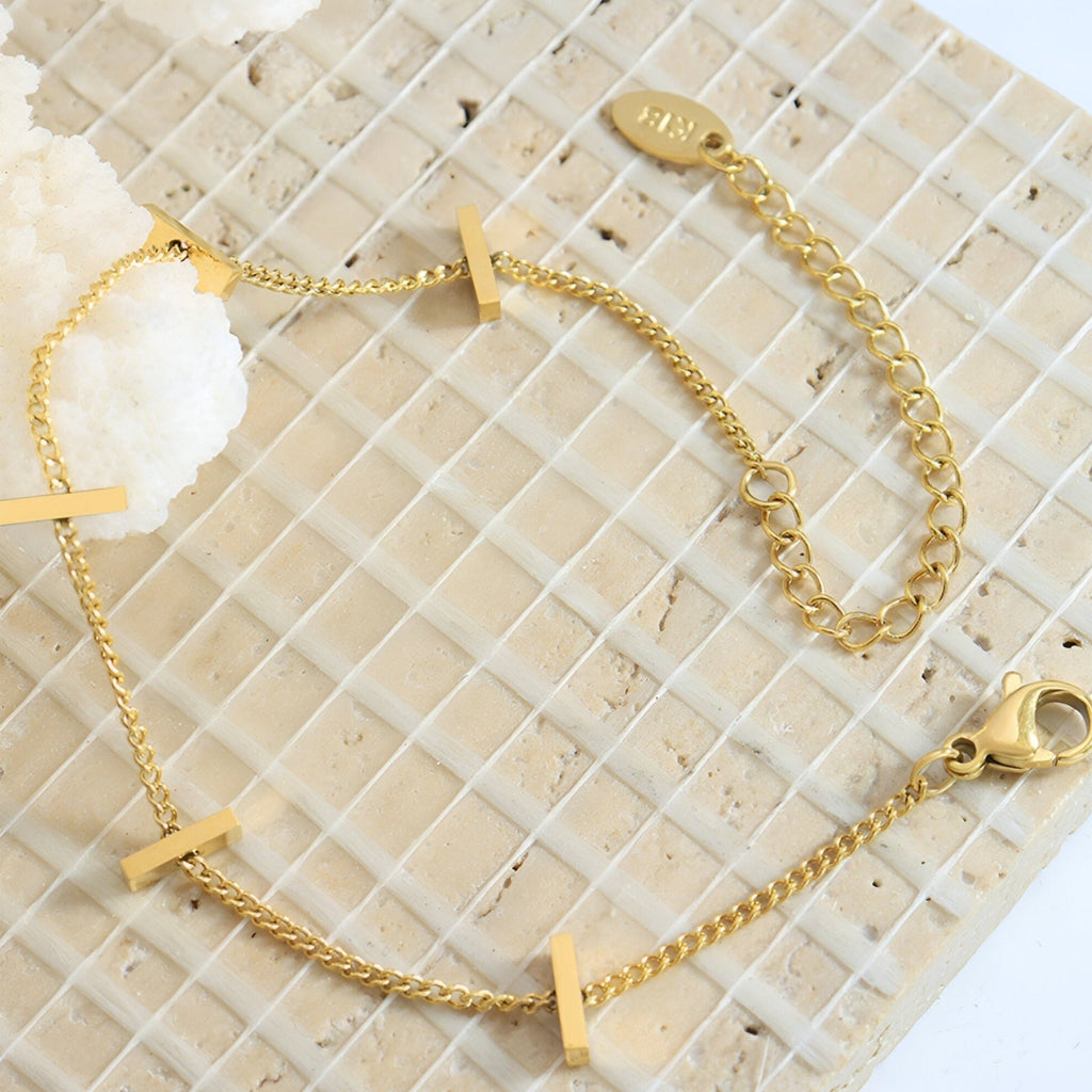 Bracelet fin plaqué or en titane avec trois barrettes horizontales sur chaîne délicate.