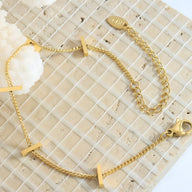 Bracelet fin plaqué or en titane avec trois barrettes horizontales sur chaîne délicate.