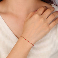 Bracelet fin doré en acier inoxydable avec perles rouges et fermeture mousqueton sur poignet féminin.