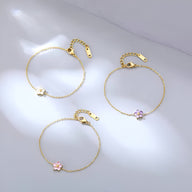 Trois bracelets en acier inoxydable doré avec pendentifs fleurs rose, violet et blanc sur chaîne fine.