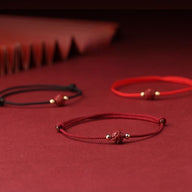 Trois bracelets fins en coton rouge, bordeaux et noir avec motif fleur de lotus cinabre et perles dorées.