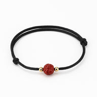 Bracelet noir en coton avec perle ronde rouge cinabre gravée fleur de lotus et petites perles dorées.