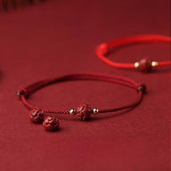 Bracelet en fil rouge avec perles cinabre sculptées et petits détails métalliques dorés.