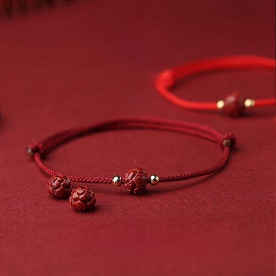 Bracelet en fil rouge avec perles cinabre sculptées et petits détails métalliques dorés.