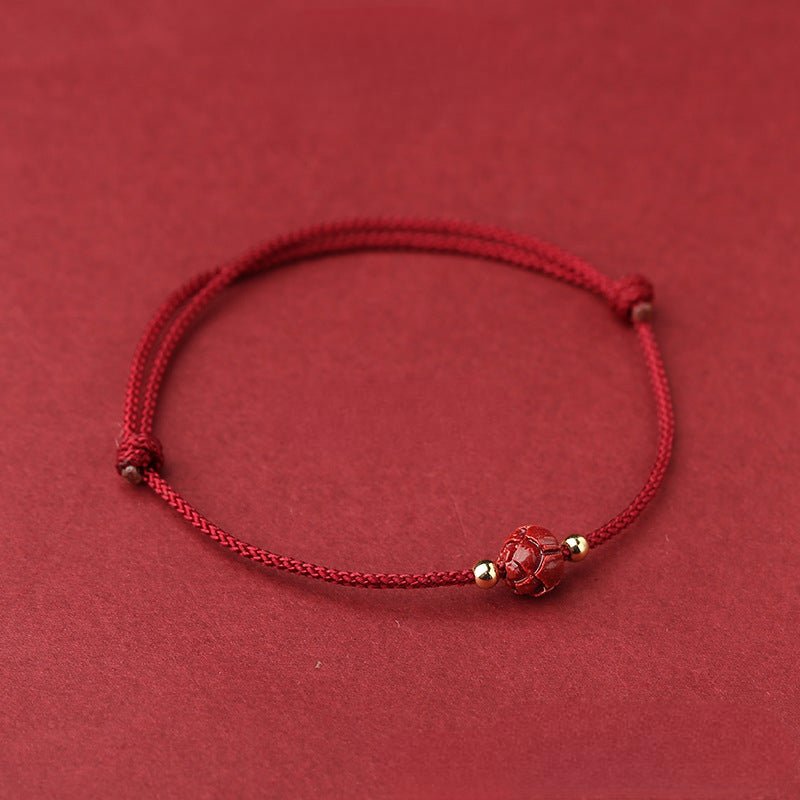 Bracelet en fil rouge cinabre avec perle fleur de lotus tissée et petits détails dorés.