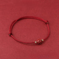 Bracelet en fil rouge cinabre avec perle fleur de lotus tissée et petits détails dorés.