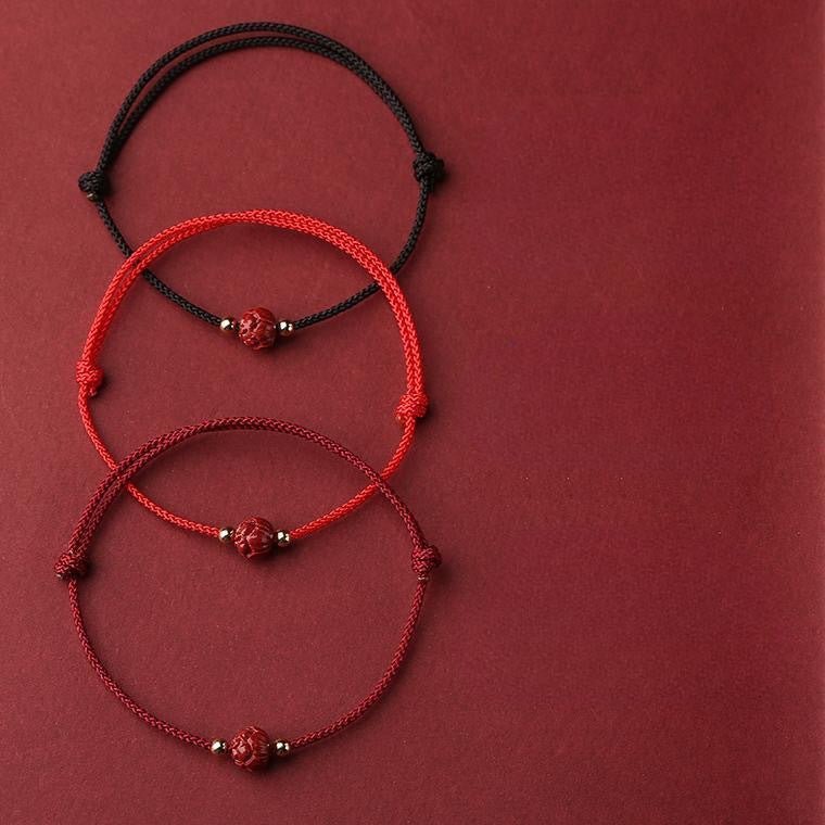 Trois bracelets en fil rouge et bordeaux avec perle cinabre rouge et fleur de lotus centrale.