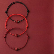 Trois bracelets en fil rouge et bordeaux avec perle cinabre rouge et fleur de lotus centrale.