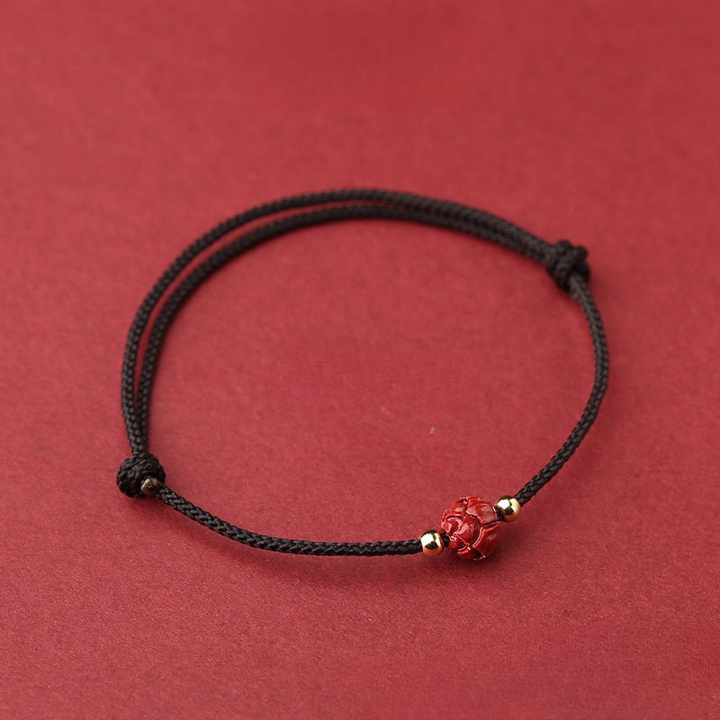 Bracelet fil rouge avec perle cinabre rouge sculptée fleur de lotus et détails dorés.
