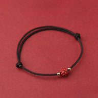 Bracelet fil rouge avec perle cinabre rouge sculptée fleur de lotus et détails dorés.