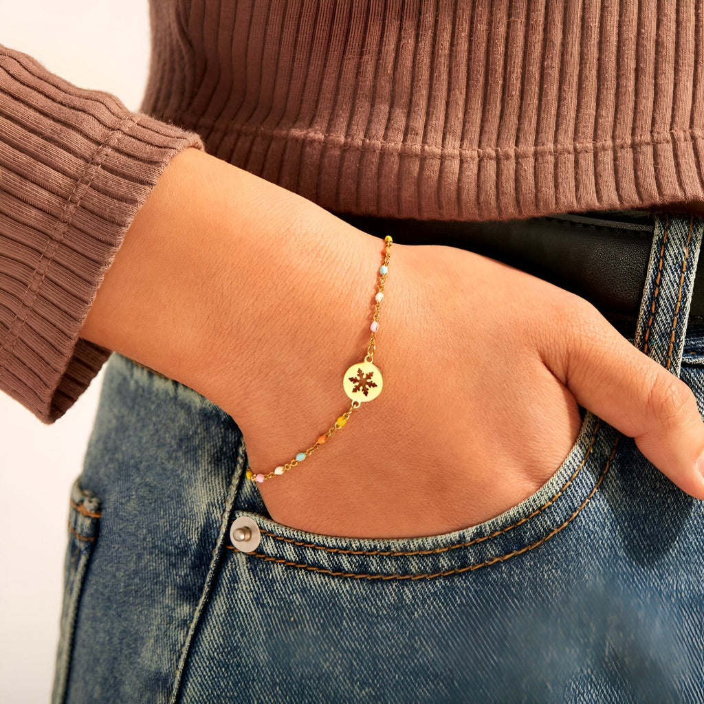 Bracelet fin en argent sterling doré avec pendentif flocon de neige porté au poignet.