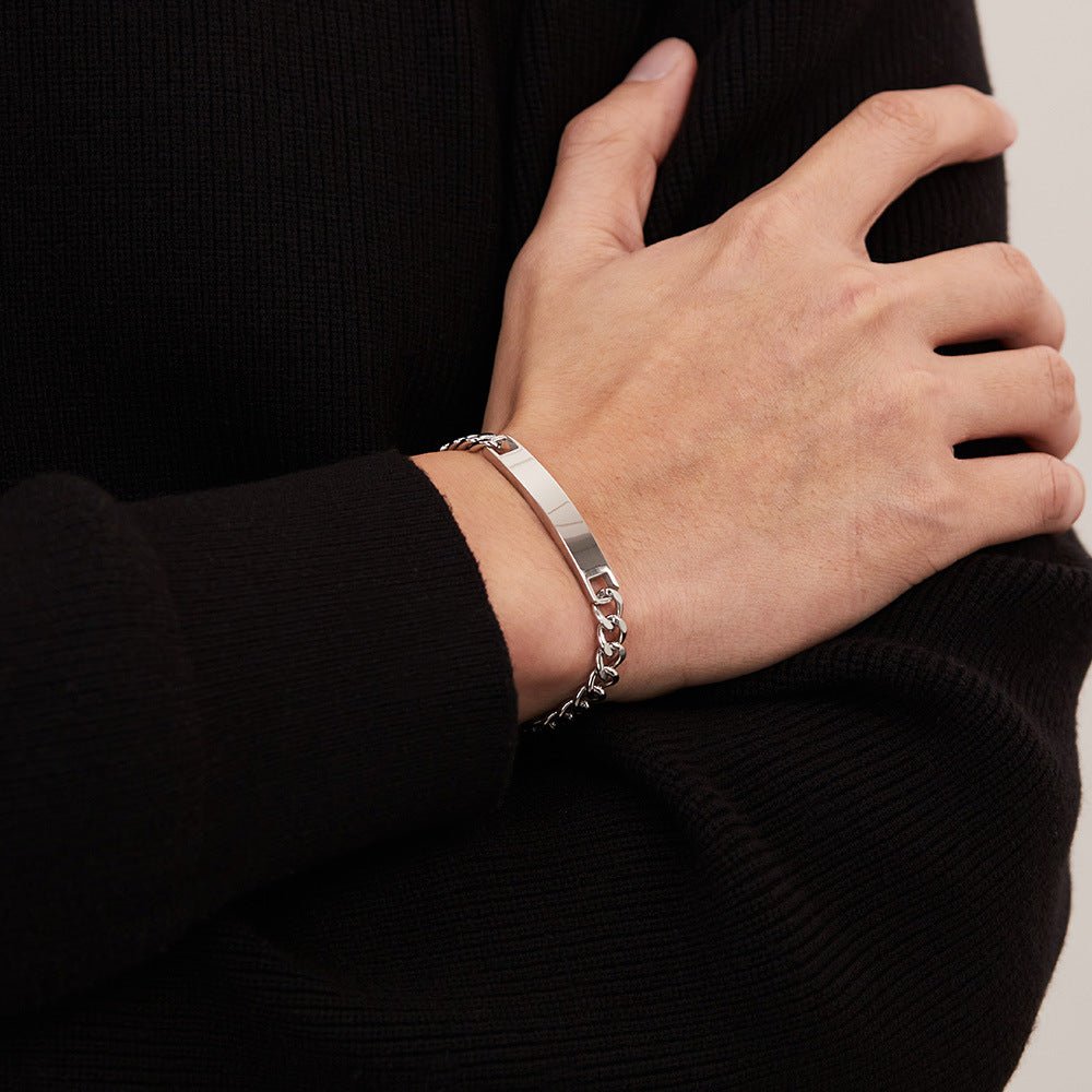 Bracelet gourmette argenté en acier inoxydable, maille cubaine, plaque personnalisable, porté au poignet masculin.