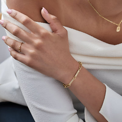 Bracelet gourmette or en acier inoxydable avec deux plaques personnalisées porté au poignet féminin.