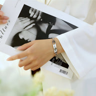 Bracelet gourmette argenté en acier inoxydable avec motifs cœurs, porté au poignet féminin.