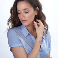 Bracelet gourmette fin en or rosé avec maillons lisses porté au poignet d'une femme en chemise bleue légère.