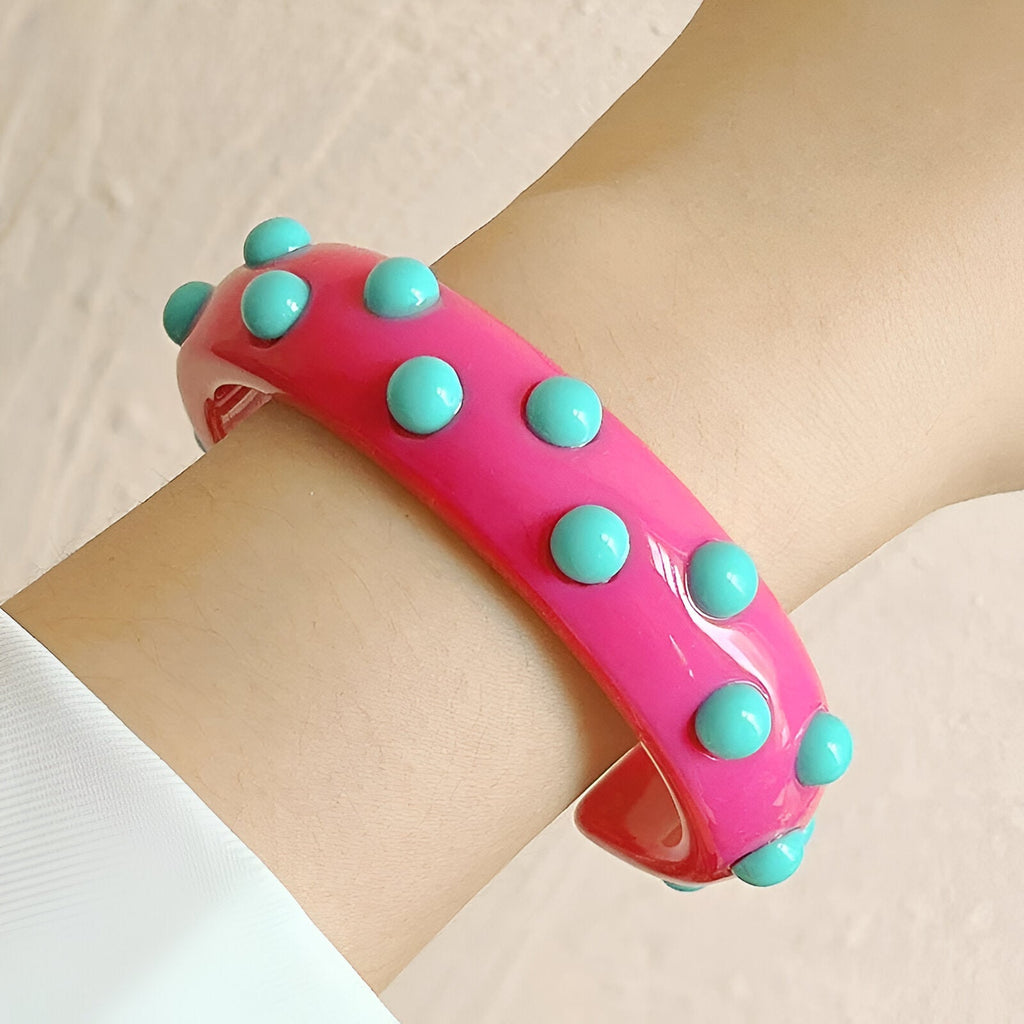 Bracelet jonc rose en résine avec breloques rondes bleu turquoise sur poignet.