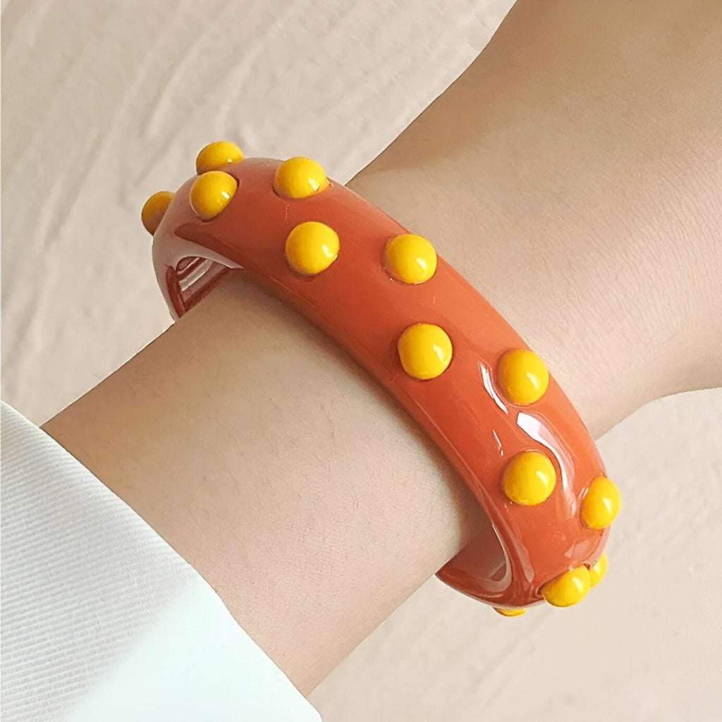 Bracelet jonc en résine orange avec pastilles jaunes en relief porté au poignet féminin.