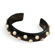 Bracelet jonc noir en résine avec petites breloques rondes blanches réparties uniformément.