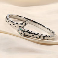 Bracelet jonc argenté en forme de léopard avec détails noirs et yeux verts étincelants.