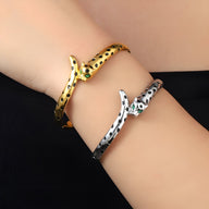 Bracelet jonc léopard doré à taches noires et bracelet jonc léopard argenté avec yeux verts sur poignet.