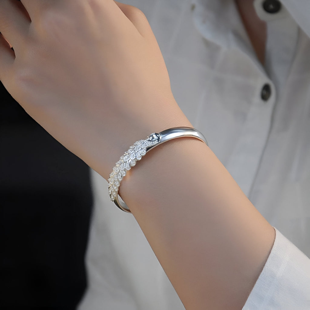 Bracelet jonc argent sterling avec motif paon détaillé porté au poignet féminin.